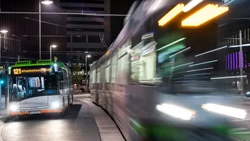 Bus steht bei Nacht an einer Haltestelle während Stadtbahn vorbeifährt.