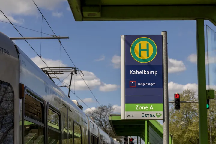 Im Fokus des Bildes ist das Haltestellenschild der Haltestelle "Kabelkamp" zu sehen. Im Hintergrund blauer Himmel mit weißen Wolken, am linken Bildrand lässt sich eine Stadtbahn erkennen.
