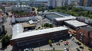 Luftaufnahme des Betriebshofes Glocksee. Im Vordergrund steht das Gebäude der technischen Verwaltung. Dahinter sieht man den Innenhof und die Hauptwerkstatt. Im Hintergrund des Bildes ist der Hauptsitz von enercity, das Ihmezentrum und die drei warmen Brüder zu sehen.