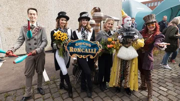 Artisten des Zirkus Roncalli stehen gemeinsam mit ÜSTRA Vorständin van Zadel auf dem Betriebshof.