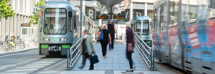 Several people on a high-level platform in Hannover. Light rail trains can be seen on both sides of the image.