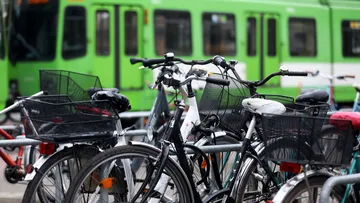 Im Vordergrund stehen mehrere abgestellte Fahrräder, im Hintergrund fährt eine grüne Stadtbahn des TW 6000 vorbei.