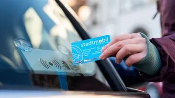 Nahaufnahme auf eine Hand, die eine stadtmobil-Karte im Scheckkartenformat an die Windschutzscheibe eines stadtmobil-Autos hält, um es zu entriegeln.