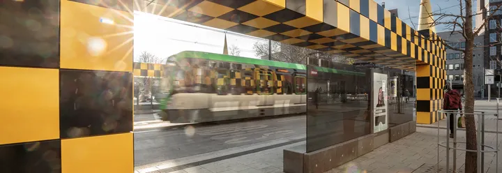 Darstellung der Haltestelle Steintor in Hannover, mit einer besonderen Bushaltestelle in gelb-schwarz kariert, im Hintergrund sieht man eine vorbeifahrende Stadtbahn TW 3000