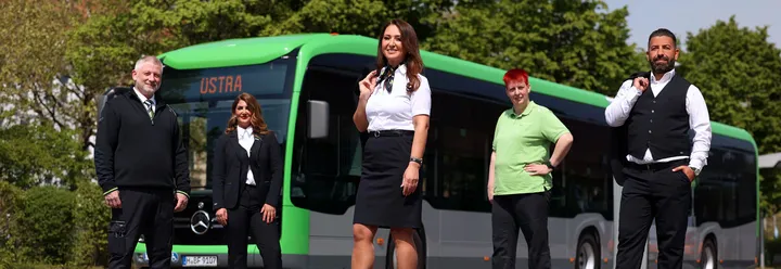 Fünf ÜSTRA Mitarbeitende in Dienstkleidung stehen vor einem Stadtbus