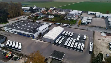 Eine Luftaufnahme des Betriebshofes Eldagsen. Links sieht man die Bushalle, rechts sind Busse neben- und hintereinander abgestellt. Im Hintergrund sind Felder zu sehen.