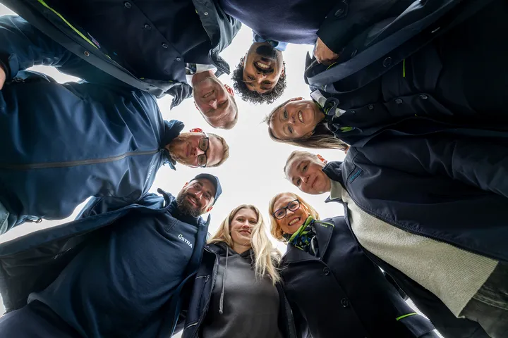 Acht Mitarbeiter*innen von ÜSTRA und regiobus stehen eng nebeneinander im Kreis und schauen lachend in die Kamera am Boden.a