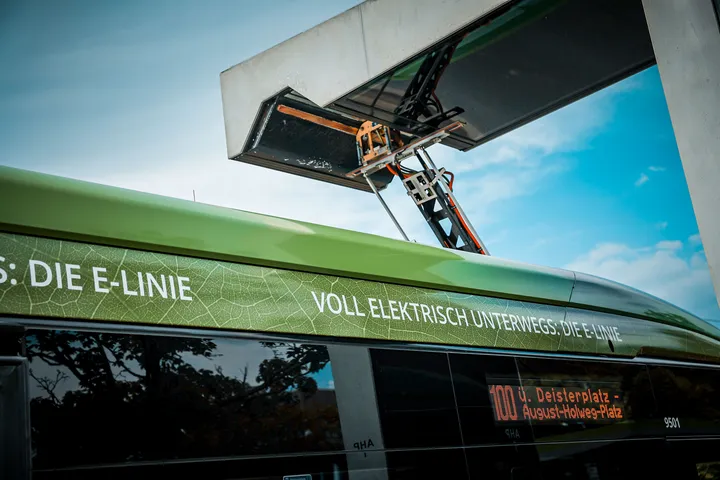 Ein Pantograph eines Elektrobusses ist ausgefahren und lädt an einer Ladesäule.