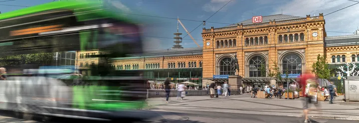 Ein ÜSTRA Bus fährt von links ins Bild, er ist verschwommen. Im Hintergrund sind der Hauptbahnhof Hannover und Menschen zu sehen.