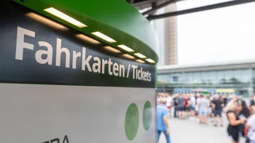 Links im Bild ist der obere Teil von einem ÜSTRA Fahrkartenautomat zu sehen. Im Hintergrund sind viele Menschen zu sehen, die verschwommen sind.