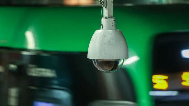 Überwachungskamera in einer Station, im Hintergrund ist eine grüne Stadtbahn der Linie 5 zu sehen.