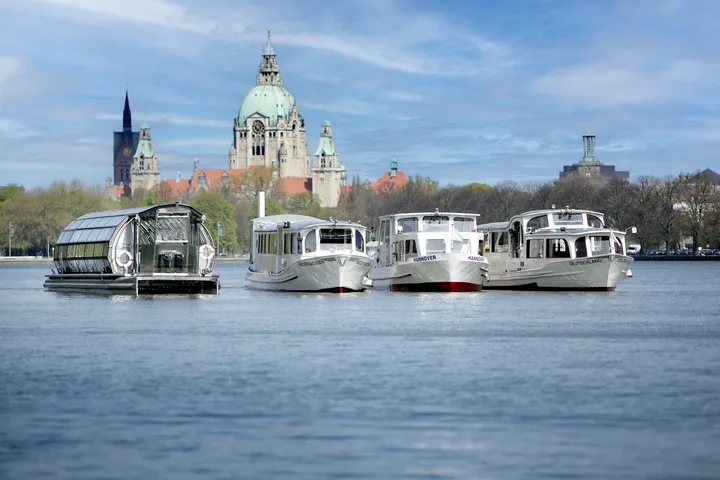 Die vier Boote der Maschseeflotte nebeneinander auf dem Wasser, im Hintergrund die Skyline von Hannover mit dem neuen Rathaus.