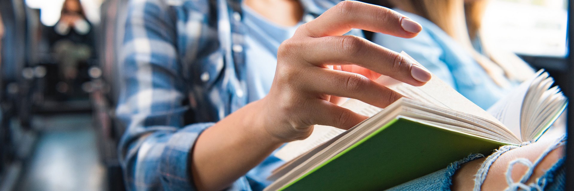 Eine Frau sitzt in einem Bus und blättert mit ihrer linken Hand in einem Buch.