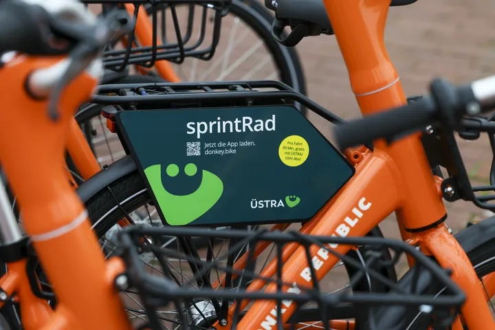 Nahaufnahme auf orangefarbige Sprinträder. Im Fokus des Bildes ist ein dunkelgrünes Schild, das an einem Gepäckträger montiert ist mit der Aufschrift "sprintRad" und dem hellgrünen ÜMO.