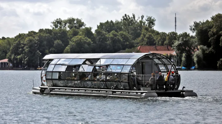 Der Solar-Katamaran EMS Europa auf dem Maschsee in Hannover. Im Hintergrund sieht man Bäume, blauen Himmel und weiße Wolken.