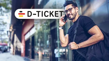 Männlicher, telefonierender Fußgänger in der Innenstadt vor einer Ladenzeile und Signet des Deutschlandtickets
