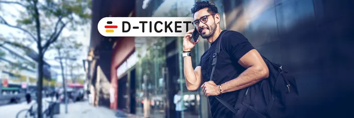 Männlicher, telefonierender Fußgänger in der Innenstadt vor einer Ladenzeile und Signet des Deutschlandtickets