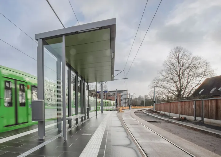 Der Hochbahnsteig mit Wartehäuschen der Haltestelle Riechersstraße im Regen. Ein TW 6000 fährt ein.