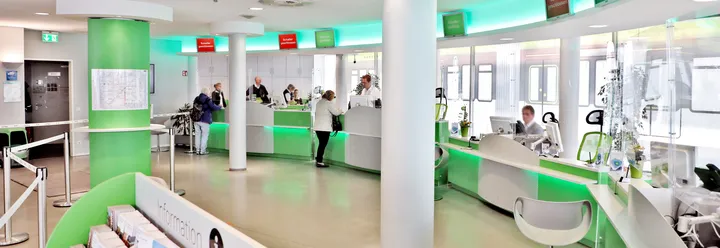 Auf dem Foto ist der Innenraum des ÜSTRA Servicecenters mit Ticketschaltern dargestellt. ÜSTRA Mitarbeiter sitzen hinter den Schaltern und warten auf Kund*innen.