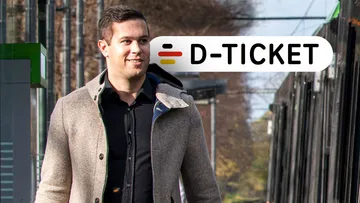 Mann läuft entlang Bahnsteig mit Deutschlandticket im Hintergrund