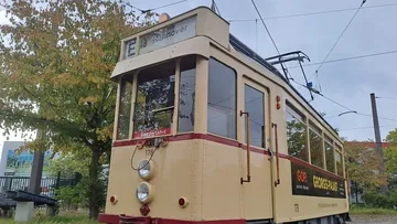 Ein alter Stadtbahnwagon auf Gleisen, im Hintergrund sind Bäume und blaugrauer Himmel zu sehen.