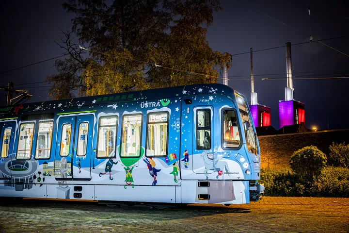 Winterbahn 2024 steht beleuchtet vor den ebenfalls bunt beleuchteten drei warmen Brüdern in Hannover