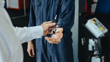 Mann im Hemd übergibt in einer Werkstatt seinen Autoschlüssel an einen Mann im Blaumann