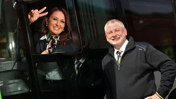 ÜSTRA Mitarbeiterin sitzt in Fahreug und zeigt Peace-Symbol. Ihr Kollege steht daneben und lächelt. Beide tragen Dienstkleidung.