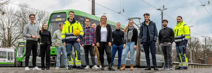 ÜSTRA Azubis und Duale Studenten stehen auf dem Betriebshof Glocksee vor Stadtbahnen des Typs TW3000 und lächeln in die Kamera