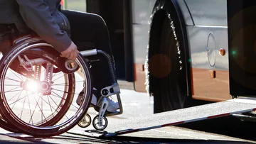Eine Person im Rollstuhl, die über die ausgefahrene Rampe in einen Bus fährt. Im Fokus des Bildes sind Rollstuhl und Rampe, Person und Bus sind nur abgeschnitten zu sehen.