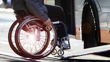 Eine Person im Rollstuhl, die über die ausgefahrene Rampe in einen Bus fährt. Im Fokus des Bildes sind Rollstuhl und Rampe, Person und Bus sind nur abgeschnitten zu sehen.