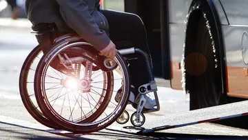 Eine Person im Rollstuhl, die über die ausgefahrene Rampe in einen Bus fährt. Im Fokus des Bildes sind Rollstuhl und Rampe, Person und Bus sind nur abgeschnitten zu sehen.