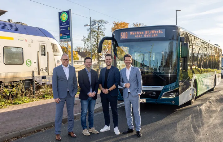 Bei dem Pressetermin in Weetzen verkünden Regionspräsident Steffen Krach, Verkehrsdezernent Ulf-Birger Franz und Vertreter der Gemeinde die Verlängerung zum Bahnhof Weetzen. Sie stehen vor dem Bus, im Hintergrund kann man eine S-Bahn sehen.