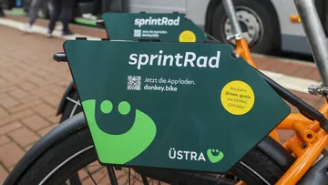 Zu sehen ist ein Bus in Hannover und davor stehen die orangenen ÜSTRA sprintRäder von Donkey Republic