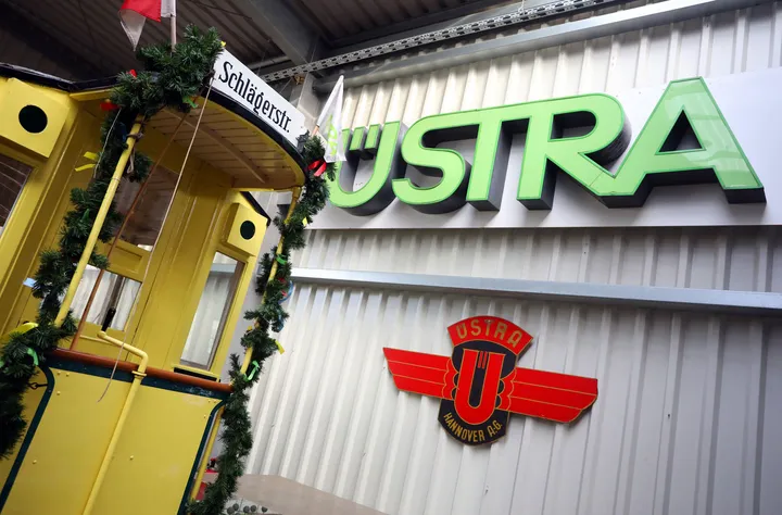 Ein Garagentor mit altem ÜSTRA Schriftzug. Im Anschnitt ist eine alte Stadtbahn mit Zugziel "Schlägerstraße" zu sehen. Die Stadtbahn ist mit einer grünen Tannengirlande und bunten Schleifen dekoriert.