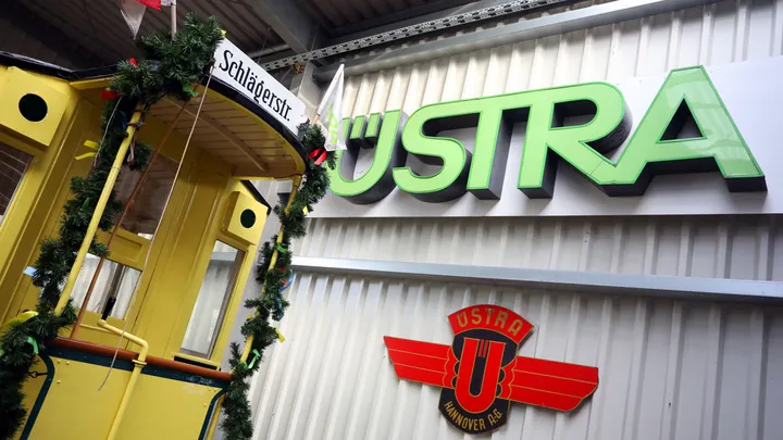 Ein Garagentor mit altem ÜSTRA Schriftzug. Im Anschnitt ist eine alte Stadtbahn mit Zugziel "Schlägerstraße" zu sehen. Die Stadtbahn ist mit einer grünen Tannengirlande und bunten Schleifen dekoriert.