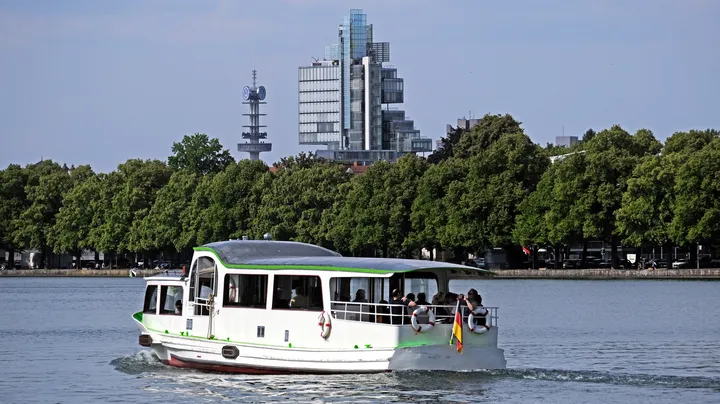 Das Schiff EMS Deutschland auf dem Maschsee, im Hintergrund sind grüne Bäume, blauer Himmel und das Gebäude der Nord LB zu sehen.