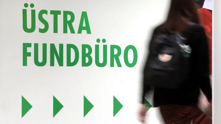 Eine Person geht ins Fundbüro der ÜSTRA. An der Wand weisen Pfeile den Weg. Darüber steht "ÜSTRA Fundbüro".