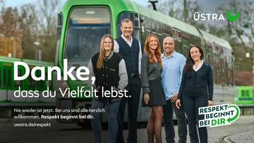 Mehrere Mitarbeitende der ÜSTRA stehen lächelnd vor einer Stadtbahn.