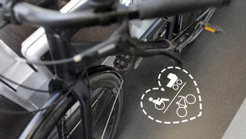 Close-up bird's-eye view of a bicycle parked in the multi-purpose area of a light rail vehicle. The multi-purpose area is marked with a dotted heart symbol depicting a wheelchair, a stroller, and a bicycle.