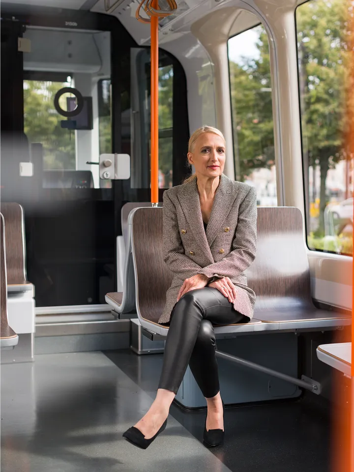 Regine Oelfke sitzt mit überschlagenen Beinen in einer Stadtbahn und blickt in die Kamera