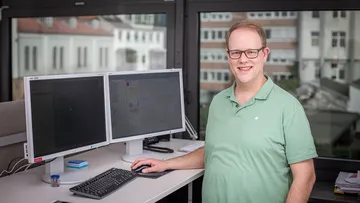 IT-Mitarbeiter der ÜSTRA steht vor Schreibtisch mit zwei Bildschirmen