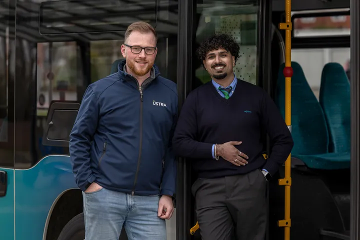 Zwei junge Männer stehen in Dienstkleidung von ÜSTRA und regiobus vor einem Linienbus.