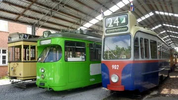 Drei alte bunte Stadtbahnen nebeneinander in einer Halle. Die linke Bahn ist gelb, die mittlere knallgrün und die rechte blau-rot.