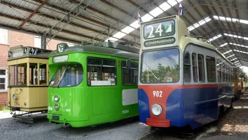 Drei alte bunte Stadtbahnen nebeneinander in einer Halle. Die linke Bahn ist gelb, die mittlere knallgrün und die rechte blau-rot.
