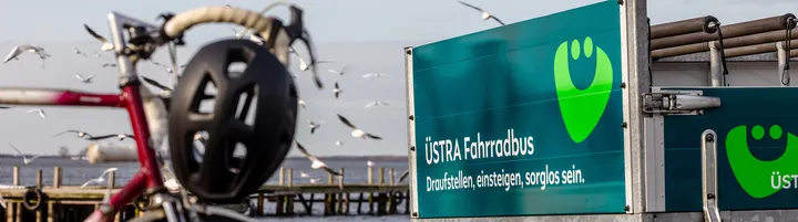 Ein Rennrad links im Bild, der ÜSTRA Fahrradbus-Anhänger rechts im Bild, im Hintergrund sieht man das Steinhuder Meer und einige Möwen.