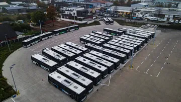 Eine Luftaufnahme des Betriebshofes Neustadt. Man sieht viele Busse hintereinander und nebeneinander abgestellt auf einem halbrunden Parkplatz. Im Hintergrund ist ein Gewerbegebiet.