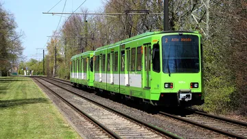 Ein grüner T W 6000 fährt als Linie 2 in Richtung Alte Heide. Neben den Gleisen ist eine frisch gemähte Wiese und knospende Bäume und Büsche.