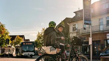 Zwei Menschen stehen mit Fahrrädern an einer Bushaltestelle